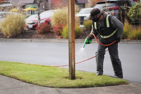 Technician in hi vis applying treatment at a parking island.